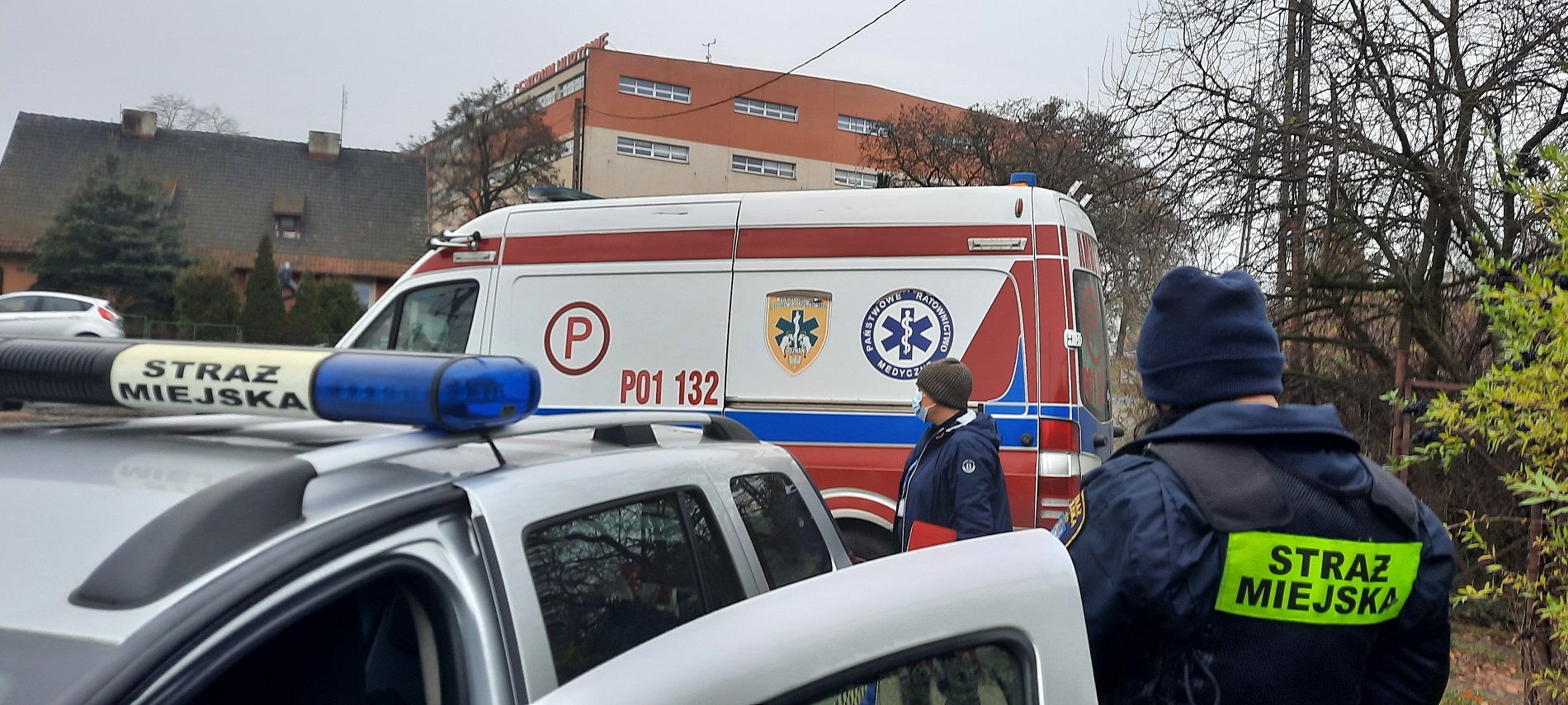 Zdjęcie przed altaną - radiowóz Straży Miejskiej, ambulans Zespołu Ratownictwa Medycznego oraz strażniczka i pracownica socjalna - grafika artykułu