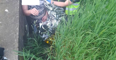 Strażniczka Referatu Interwencyjno - Drogowego podczas udzielania pierwszej pomocy przedmedycznej - mężczyna owinięty kocem termicznym jest przygotowywany do wyciągnięcia na drogę