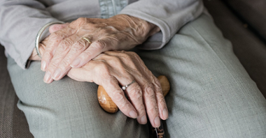 Zdjęcie przedstawią starszą osobę trzymającą w dłoniach laskę.